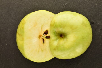 Two halves of a ripe green apple on a slate board, close-up, top view.
