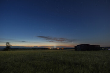The Neowise comet in the night sky over meadow with wooden barn in morning twilight before sunrise...
