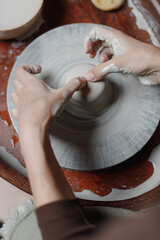 top view women's hands on a potter's wheel creates utensils of gray eco-friendly clay in their own workshop. The result of creative activity for sale. Own creative business.