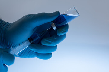 Scientist's hand wearing blue gloves and holding an ampoule and syringe. Coronavirus or influenza vaccination concept. Vaccine development concept