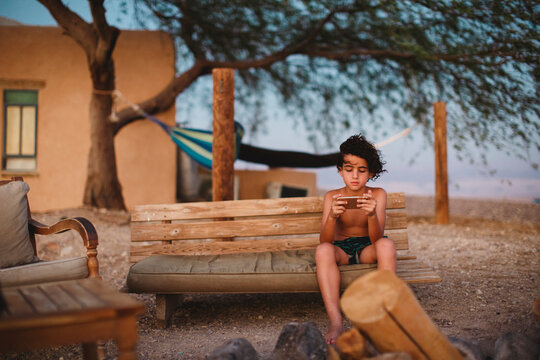 A young boy playing with his smartphone sitting on a bench in desert