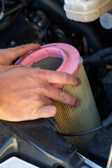 close up of hands of a caucasian male car mechanic changing the air filter in an engine