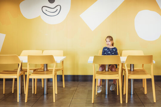 Young girl sitting at table and chairs with colorful background