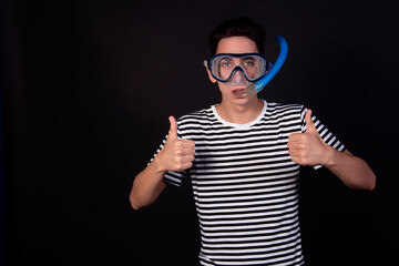 Funny young man in a sailor suit. Diving mask and snorkel. Striped clothing. Black background.