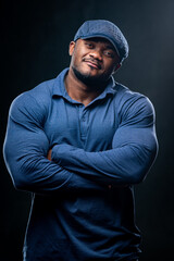 Obraz premium Confident smiling man holds hands crossed. Photo of african man in casual outfit on black background.