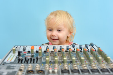 A little girl is indulging next to a mixing console in a music studio.