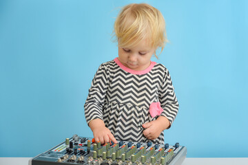 A little girl is indulging next to a mixing console in a music studio.