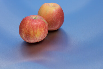 two fresh delicious apples and reflection on blue clean metallic background