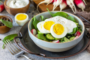 Fresh spring food, healthy vegan lunch bowl. Spinach, cucumber, radish salad and boiled eggs with sour cream.