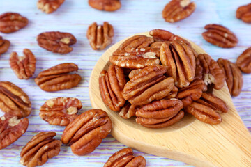 Pile of Pecan Nuts on Wooden Ladle with Many Kernels Scattered on Pale Blue Wooden Table