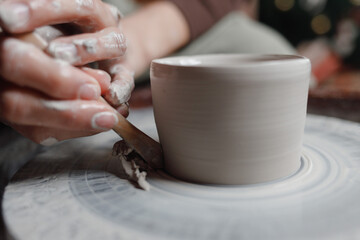 Closeup of potter's hands molds clay pot spinning on pottery wheel with special wooden tool. Woman works with tools in pottery workshopCloseup of potter hands molds clay pot spinning on pottery whee