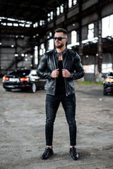 Stylish handsome man with sunglasses in fashionable clothes stands with the luxury black car on the background. Closeup.