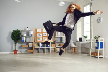 Overjoyed employee leaving office at the end of day. Young man having fun as it's time to finish work. Funny white-collar worker is so happy that workday is over that is jumping high ready to fly home