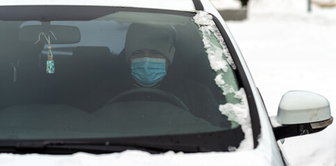 Fototapeta premium A man sits in a car wearing a virus-protective mask close-up