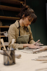 A young Caucasian woman makes sides with her hands for a plate of clay in a pottery workshop. Beautiful dishes with their own hands. Manual labor. Creative masterclass