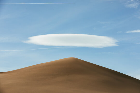 single sand dune with a single white cloud and chem trails