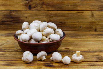 Fototapeta na wymiar Fresh champignon mushrooms in ceramic bowl on the wooden table