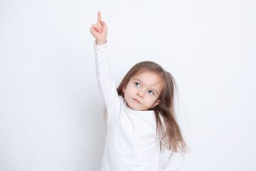 Fototapeta premium Portrait of a girl on a white background with her hand and finger raised up. Blue eyes. Russ hair. Bright tones. Points up