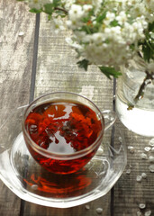 Hawthorn spring floral tea with spring blooming branches with flower buds on wooden background, focus on the blossom reflection in the tea, closeup, copy space, vertical, herbal teas  concept