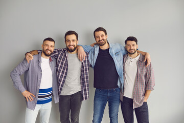 Group of cheerful friends having fun together. Portrait of happy bearded young men standing with arms around each other's shoulders and smiling at camera in studio with light gray background - Powered by Adobe