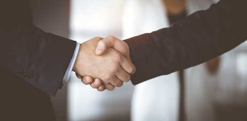 Obraz premium Unknown businesspeople are shaking their hands after signing a contract, while standing together in a sunny modern office, close-up. Business communication, handshake, and marketing concept