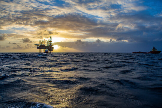 Offshore drilling platform during sunrise with work vessel