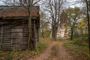 A path strewn with dry, fallen leaves leads to an abandoned, dilapidated temple. Nearby is an old log shed.