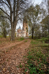 A path strewn with dry, fallen leaves leads to an abandoned, dilapidated temple.