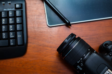 Detalhe de uma câmera fotográfica, um teclado e uma mesa digitalizadora sobre uma mesa de madeira. © Angela