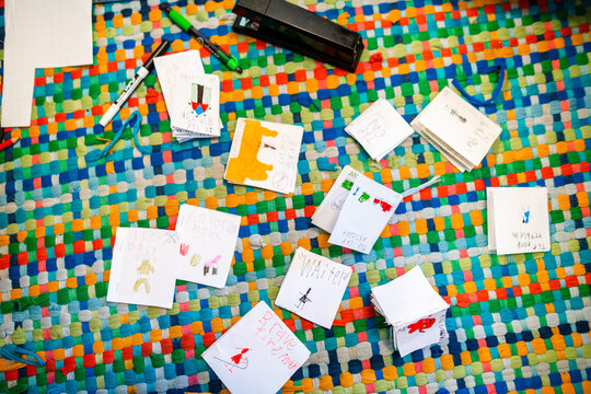 Little books created by a small child are spread across a colorful rug