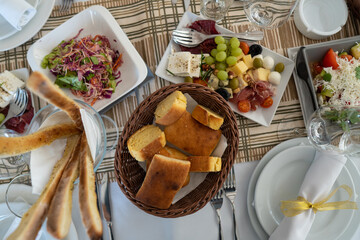 Top view of a decorative appetizer in white bowls and homemade bread in a wicker basket. Decorative food of cheese, grapes, meat, cabbage and tomatoes as part of the restaurant menu