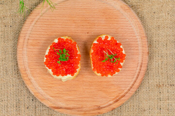 Delicious sandwiches with red caviar and butter on a wooden board against a background of herbs and mushrooms. View from above.