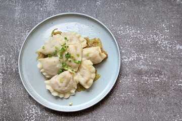 round plate, hot steaming dumplings on a fried onion pillow, carbohydrates on a plate, dumpling dough, hot dumplings sprinkled with green onions, steam over warm food