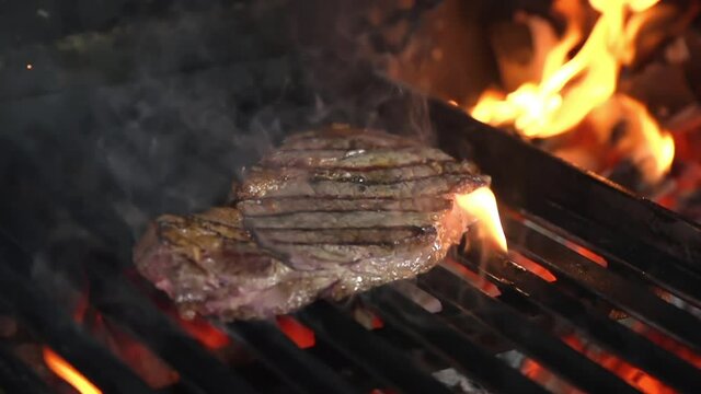 Marble steak grilled on a fire grill.
Around the steak fire smoke from below burns the fire

