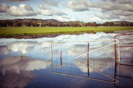 dramatic lake reflection with clouds and fence flooded gate on farm