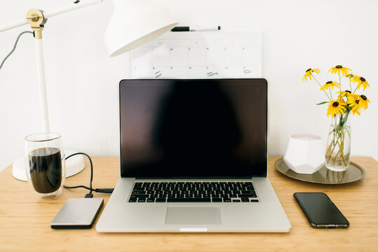 Technologies with drink and desk lamp by flower vase on wooden table in office