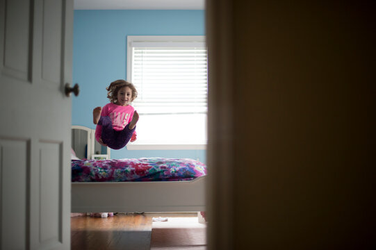 Girl jumping on bed seen through doorway at home