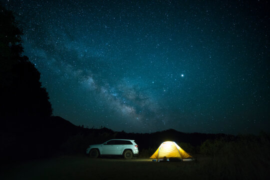 Car parked by illuminated tent against starry sky at night