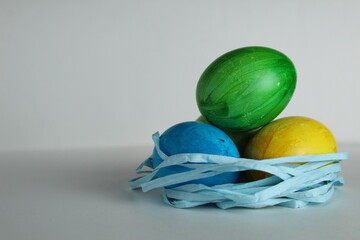 Three colored blue yellow green eggs lie in the nest on a white background with a place to text a copyspace view from the side of Von Easter