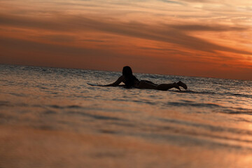 Female surfer in ocean at sunset