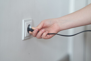 A young girl inserts a plug into an outlet. Young woman plugs the phone charger into the socket.