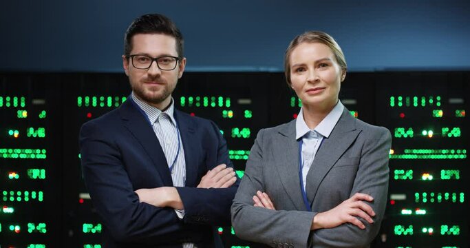 Portrait of successful programmers teammates, man with glasses and blond woman standing on background of running servers looking at camera with arms crossed.