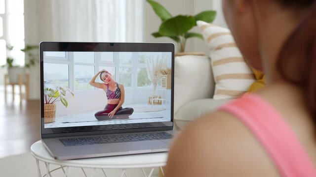 Sporty woman watching and learning exercises workout, yoga online with coach on screen of laptop computer at home