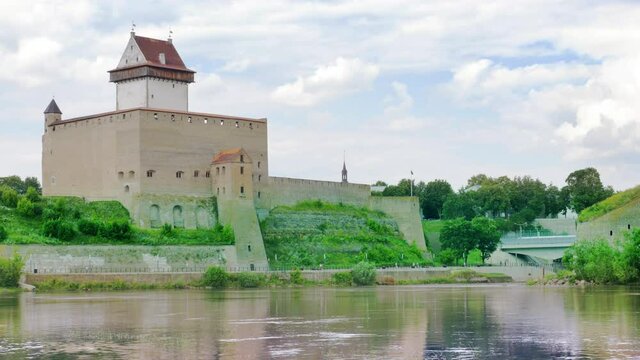 Touristic attraction city scenery, historic medieval landmark on Russian Estonian border, Narva Herman castle alongside Narva river, cloudy sky skyline