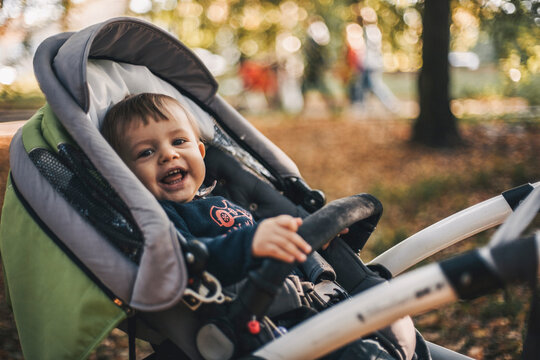 Portrait of cheerful toddler lying on baby stroller at park during autumn
