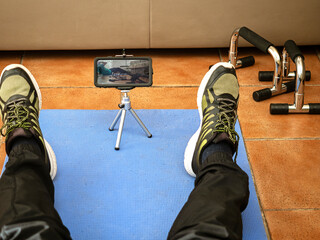 Home gym, remote training with virtual instructor. Man in sportswear sitting on the floor with a mobile phone. Concept of sports and recreation with online fitness applications.