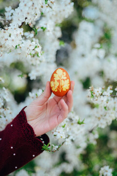 Cropped hand of woman holding Easter egg against flowers
