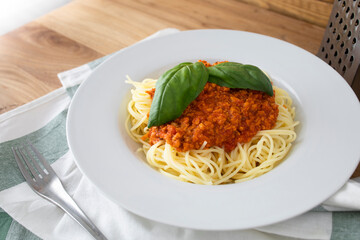 Plate of spaghetti with vegan bolognese sauce made with textured peas and decorated with some green basil leaves