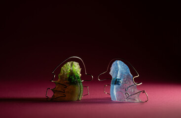 Flat view of two old dental prostheses made of green and blue plastic with metal wire. Children's dentures on a flat red background and a dark background