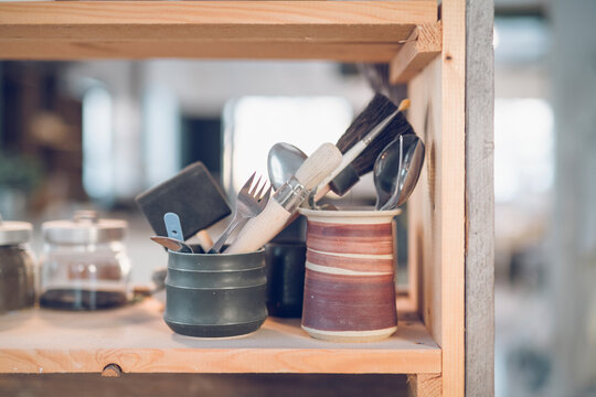 Close-up of cutleries with paintbrushes in containers on shelf at workshop